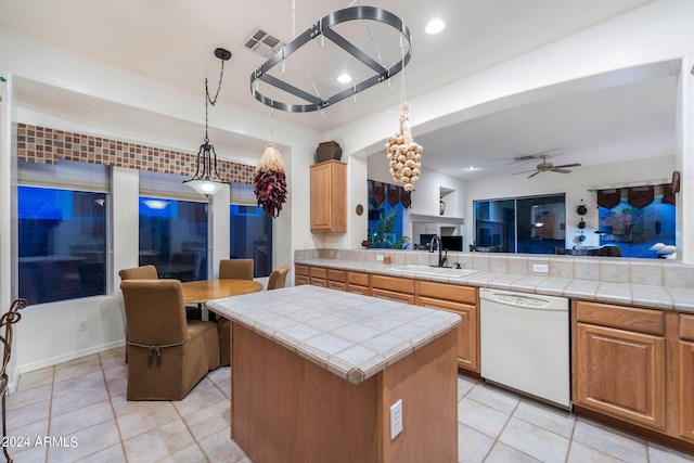 kitchen with dishwasher, sink, ceiling fan, tile counters, and a kitchen island