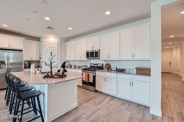 kitchen with an island with sink, light hardwood / wood-style flooring, white cabinetry, stainless steel appliances, and a kitchen breakfast bar