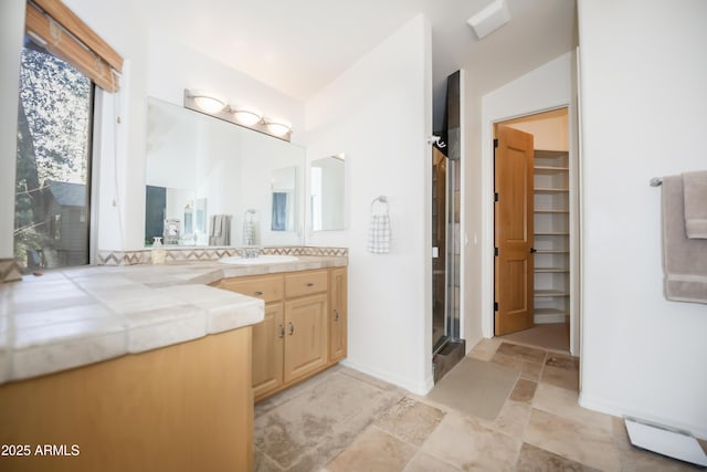 bathroom with vanity, a stall shower, baseboards, stone finish floor, and a walk in closet