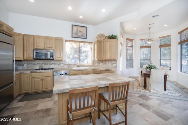 kitchen with a center island, stainless steel appliances, backsplash, light brown cabinets, and a sink