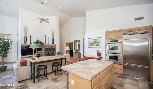 kitchen with a center island, stainless steel appliances, visible vents, light brown cabinets, and high vaulted ceiling