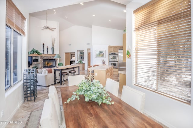 dining area featuring recessed lighting, ceiling fan, a stone fireplace, high vaulted ceiling, and baseboards