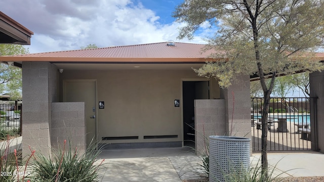 view of exterior entry with metal roof, a fenced in pool, cooling unit, concrete block siding, and fence