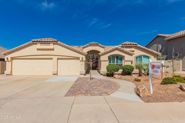 mediterranean / spanish-style home with stucco siding, driveway, an attached garage, and a tiled roof