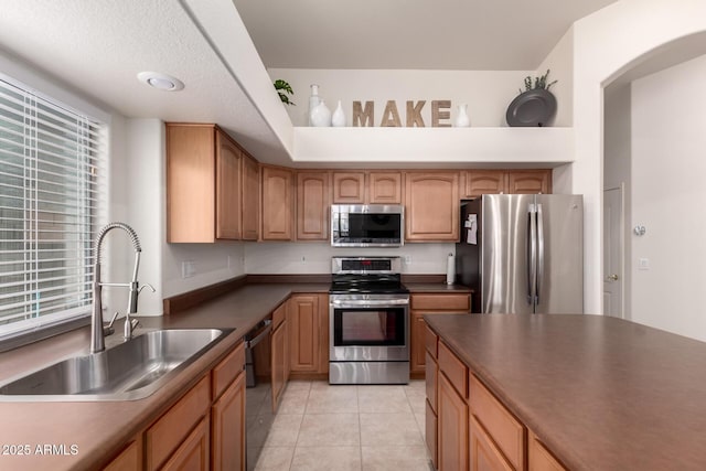 kitchen featuring a sink, dark countertops, appliances with stainless steel finishes, and light tile patterned floors