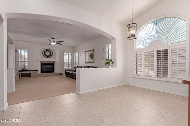 unfurnished living room featuring visible vents, light carpet, light tile patterned floors, ceiling fan with notable chandelier, and a glass covered fireplace