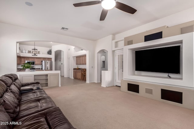 living area with arched walkways, visible vents, light colored carpet, and ceiling fan