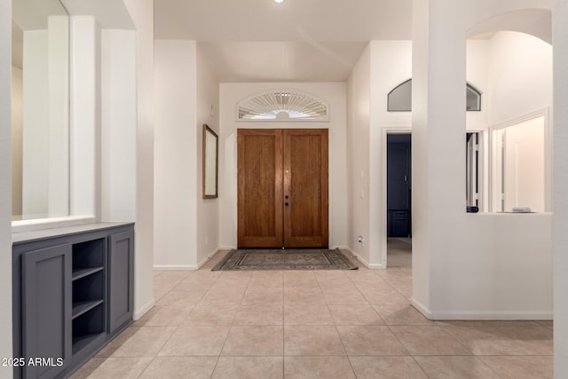 foyer featuring light tile patterned flooring, arched walkways, and baseboards