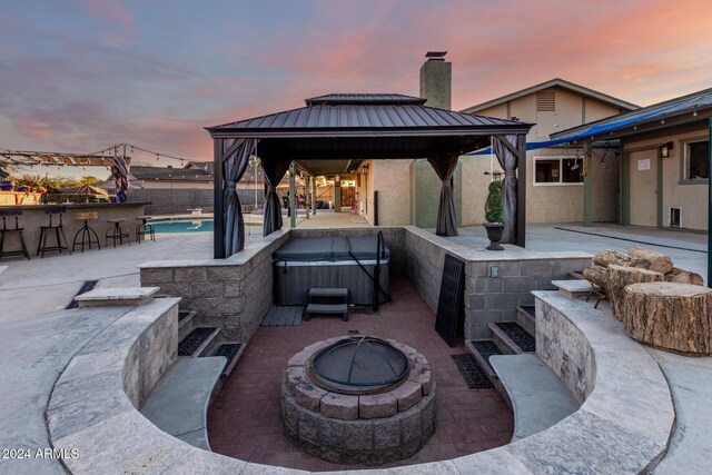 patio terrace at dusk featuring a gazebo, an outdoor bar, an outdoor fire pit, and a hot tub