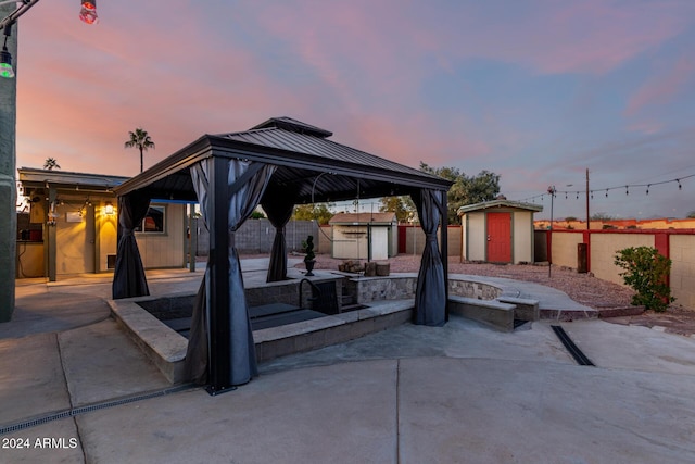 patio terrace at dusk with a gazebo, a fire pit, and a shed