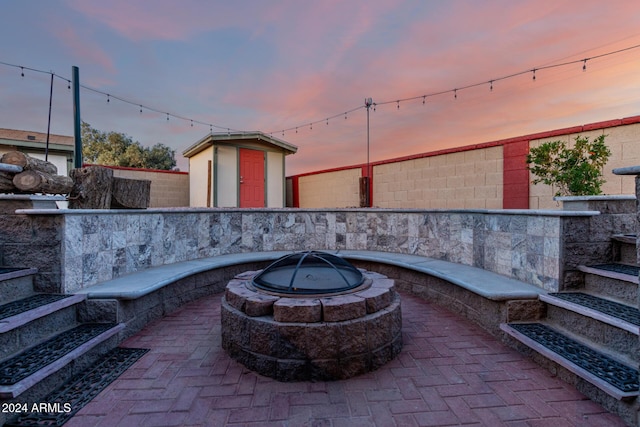 patio terrace at dusk featuring a fire pit and a storage unit