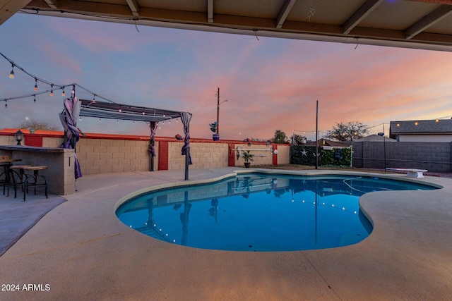 pool at dusk featuring a patio area and a bar