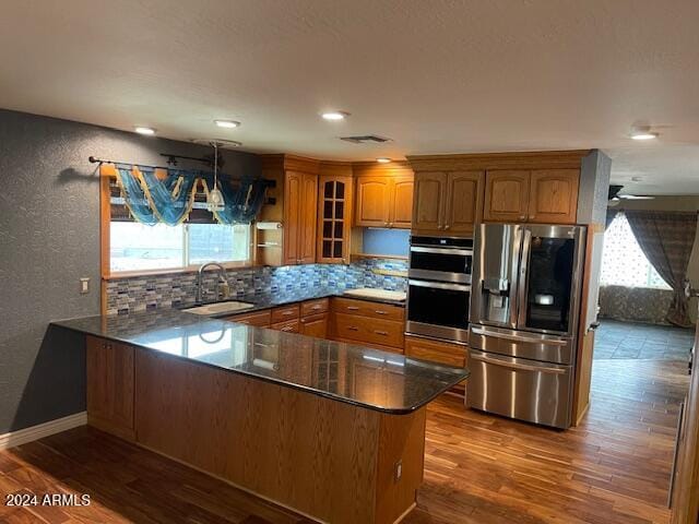 kitchen with hardwood / wood-style floors, hanging light fixtures, sink, appliances with stainless steel finishes, and kitchen peninsula