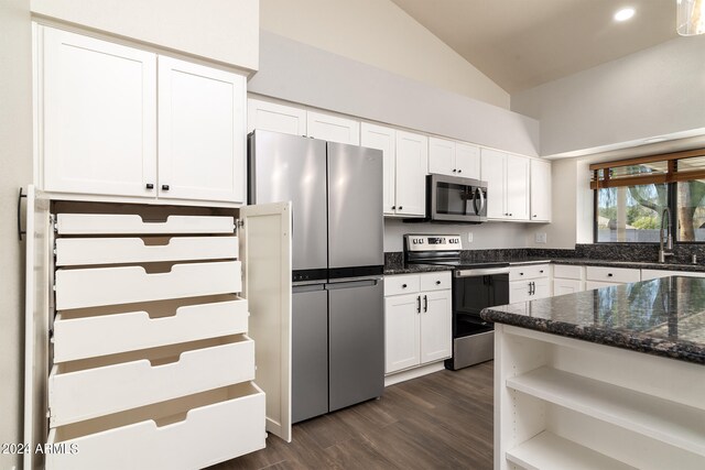 kitchen featuring appliances with stainless steel finishes, dark stone countertops, dark hardwood / wood-style flooring, white cabinets, and vaulted ceiling