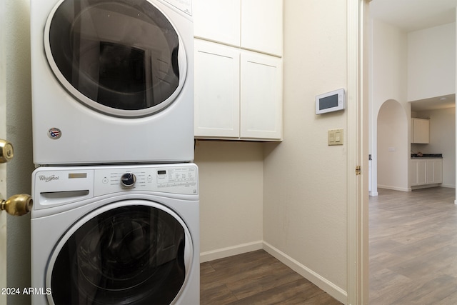 laundry room with stacked washing maching and dryer, dark wood-type flooring, and cabinets