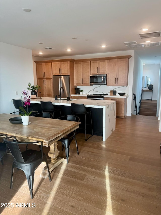 kitchen featuring sink, a breakfast bar area, an island with sink, hardwood / wood-style flooring, and stainless steel appliances