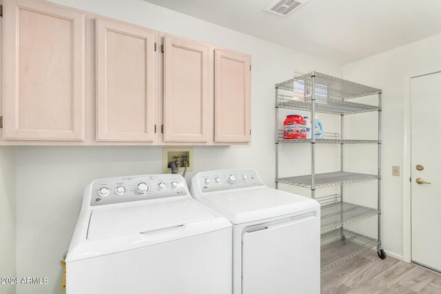 clothes washing area with cabinets, light hardwood / wood-style floors, and washer and dryer