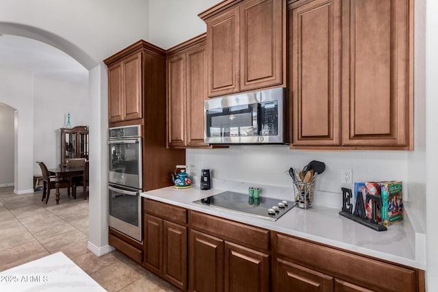 kitchen featuring stainless steel appliances, arched walkways, light countertops, light tile patterned floors, and baseboards