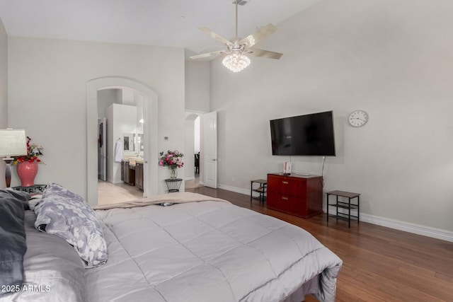 bedroom with arched walkways, wood finished floors, baseboards, a ceiling fan, and a high ceiling