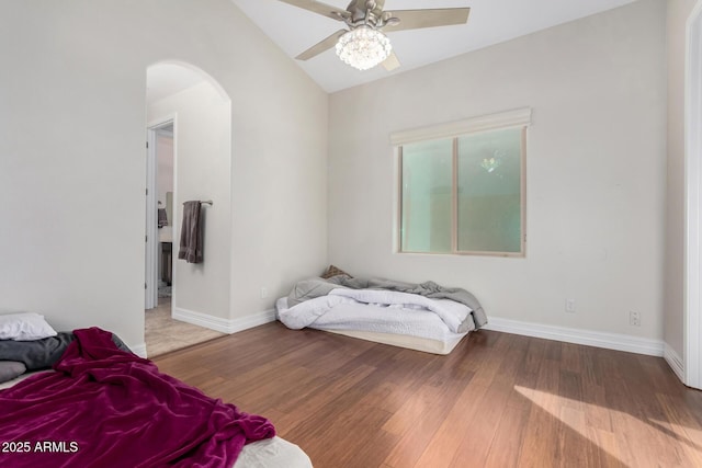 bedroom featuring arched walkways, vaulted ceiling, wood finished floors, and baseboards