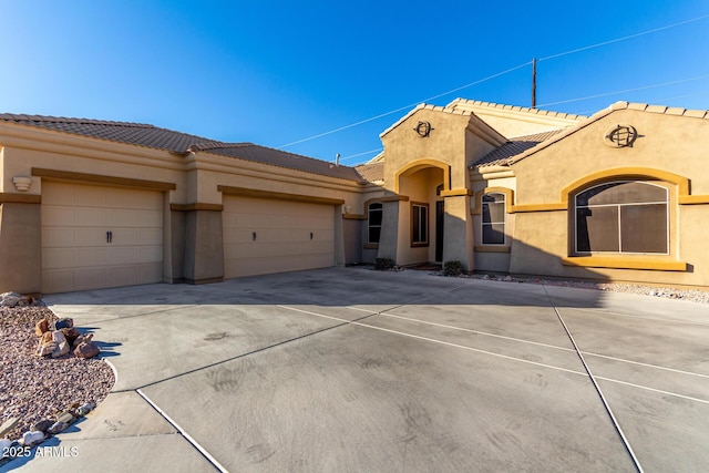 view of front facade with driveway, a tile roof, a garage, and stucco siding