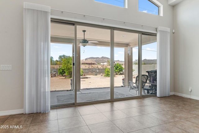doorway featuring baseboards, tile patterned flooring, a ceiling fan, and a towering ceiling