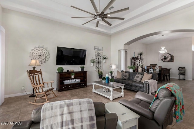 tiled living area featuring arched walkways, a ceiling fan, decorative columns, baseboards, and a raised ceiling