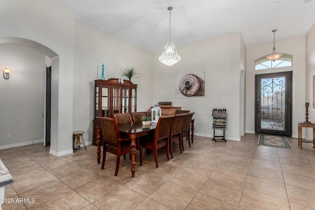 dining space featuring arched walkways, light tile patterned floors, a high ceiling, a chandelier, and baseboards