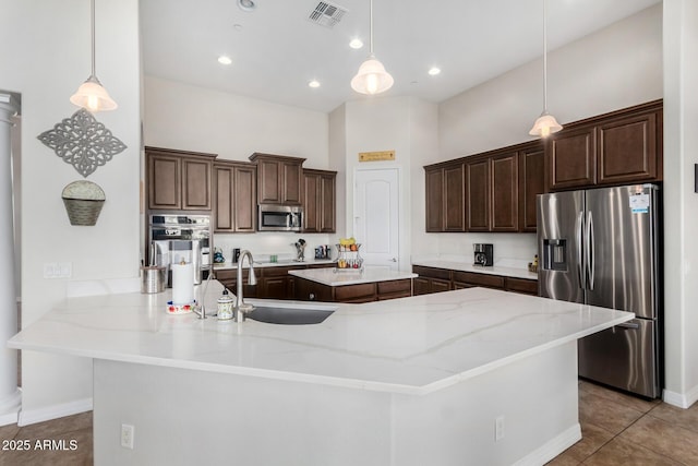 kitchen with appliances with stainless steel finishes, a sink, a kitchen island, dark brown cabinets, and tile patterned flooring