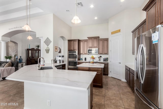kitchen with stainless steel appliances, arched walkways, a sink, a towering ceiling, and ornate columns