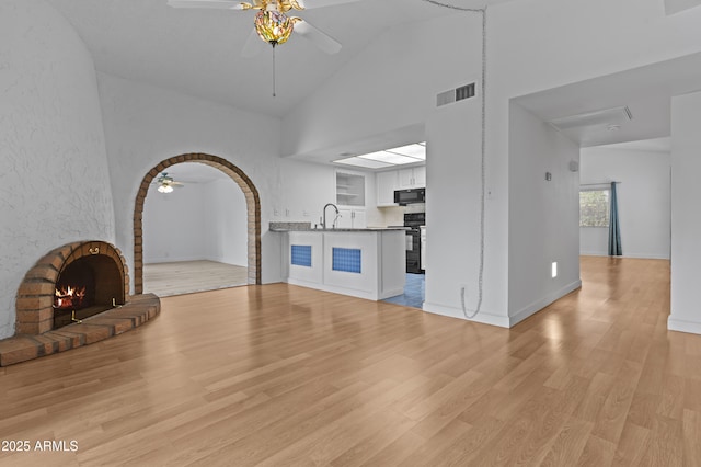 2916 S Revere Cir, Mesa, AZ 85210 - unfurnished living room featuring a ceiling fan, high vaulted ceiling, light wood finished floors, a sink, and a brick fireplace