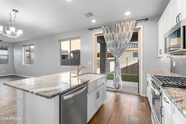 kitchen with appliances with stainless steel finishes, a center island with sink, white cabinetry, and decorative light fixtures