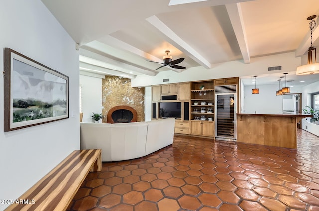 unfurnished living room with wine cooler, ceiling fan, beam ceiling, and a tiled fireplace