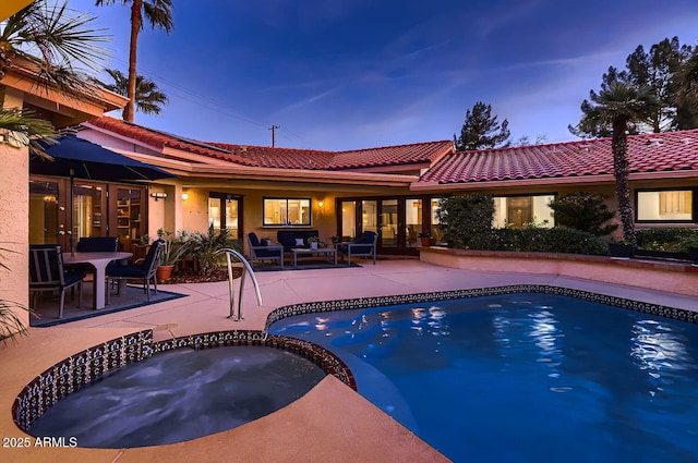 pool at dusk with an in ground hot tub and a patio area