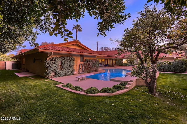 pool at dusk featuring a patio, a diving board, and a lawn