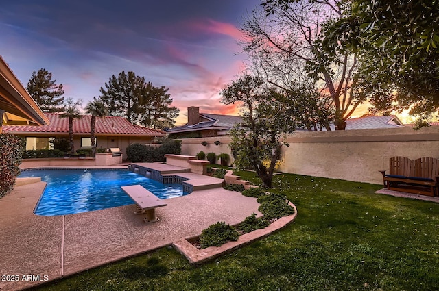 pool at dusk featuring a diving board, a patio area, pool water feature, and a lawn