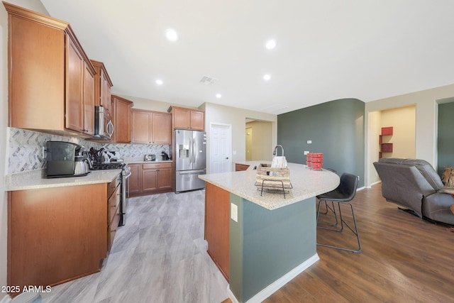 kitchen with stainless steel appliances, a breakfast bar area, a center island with sink, and light wood-type flooring