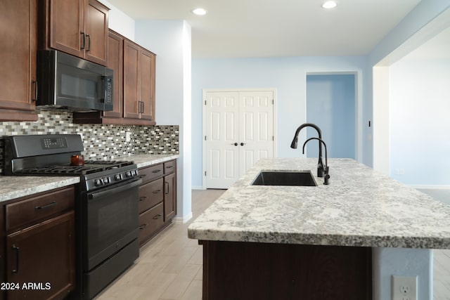 kitchen with tasteful backsplash, light stone counters, black range with gas cooktop, sink, and an island with sink