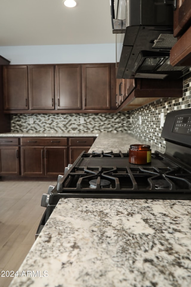 kitchen featuring dark brown cabinets, backsplash, light hardwood / wood-style floors, and exhaust hood