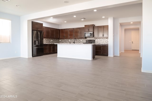 kitchen with dark brown cabinetry, stainless steel appliances, light hardwood / wood-style flooring, backsplash, and an island with sink