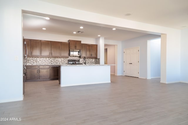 kitchen featuring tasteful backsplash, light hardwood / wood-style flooring, an island with sink, and appliances with stainless steel finishes