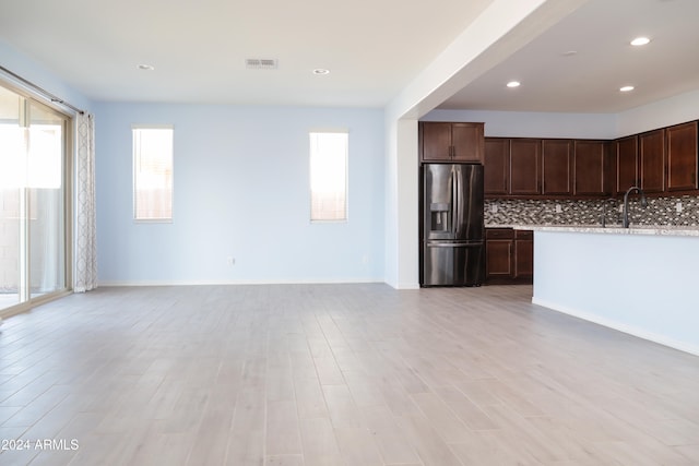 kitchen with tasteful backsplash, dark brown cabinetry, stainless steel refrigerator with ice dispenser, and light wood-type flooring