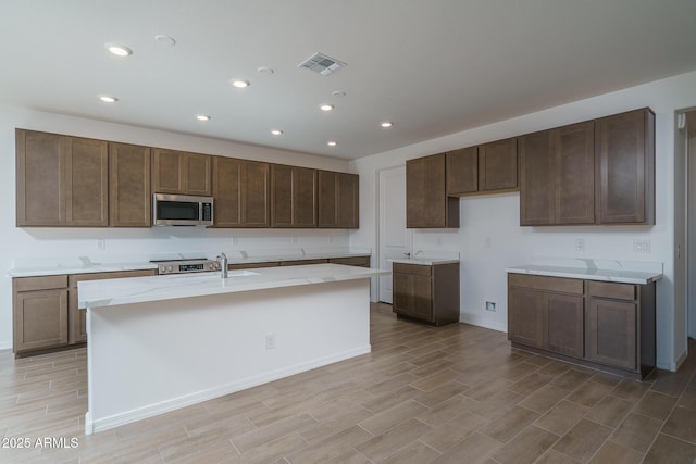 kitchen with stove, dark brown cabinetry, and an island with sink