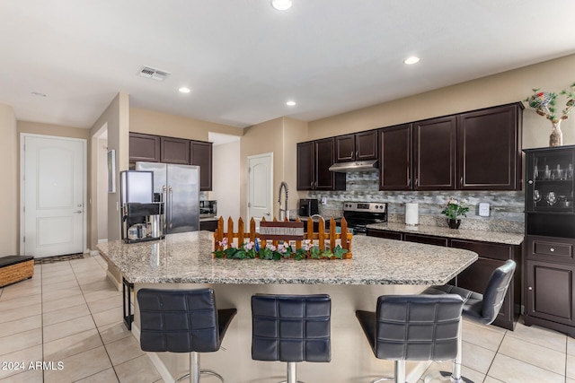 kitchen featuring stainless steel appliances, a large island with sink, a kitchen bar, decorative backsplash, and light tile patterned flooring