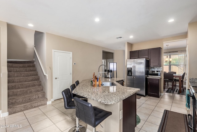 kitchen featuring sink, stainless steel refrigerator with ice dispenser, a kitchen island with sink, dark brown cabinets, and light tile patterned floors