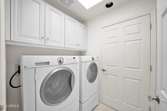 clothes washing area featuring light tile patterned floors, washing machine and clothes dryer, and cabinets