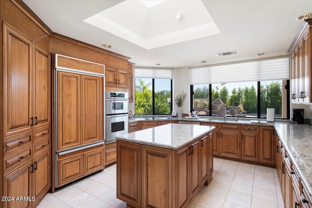 kitchen featuring light stone counters, a center island, sink, a raised ceiling, and double oven