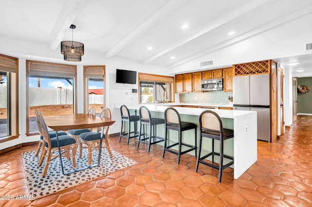 kitchen with appliances with stainless steel finishes, decorative light fixtures, vaulted ceiling with beams, a kitchen bar, and decorative backsplash