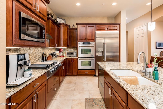 kitchen featuring light stone counters, stainless steel appliances, hanging light fixtures, backsplash, and a sink