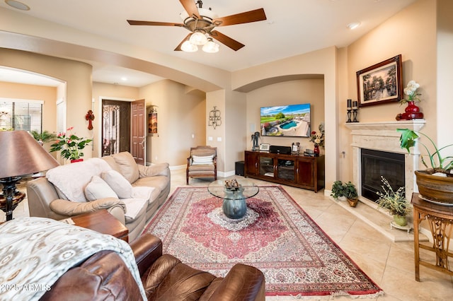 living area featuring light tile patterned floors, ceiling fan, a glass covered fireplace, and baseboards